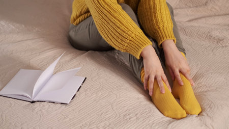 unrecognizable woman puts on cotton warm yellow sock on bed closeup. create comfort at home conceptの写真素材