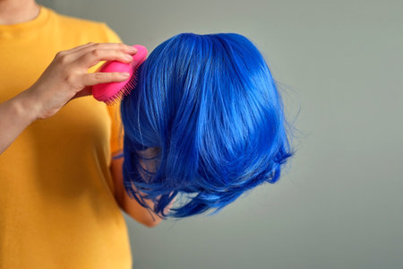 woman holds a bright wig in her hands. Womens beauty concept. unrecognizable woman combing her wig with a comb. how to check the quality of artificial hairの写真素材