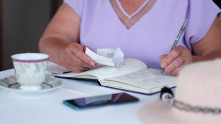 Elderly woman using a pen writing on bank account book while holding the bills to calculate. old...