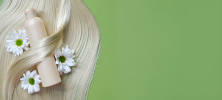 silk curls of hair and a plastic beige shampoo bottle on a green background. hair care. hair coloring conceptの写真素材