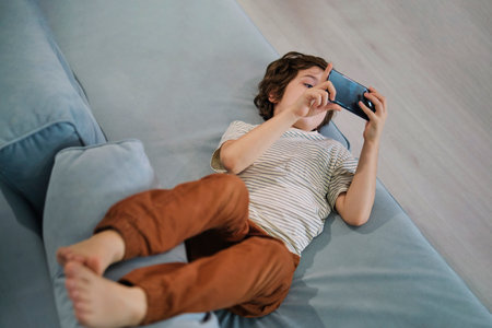 young boy lost in a digital world while lounging at home, raising questions about how parents can balance technology with physical play and human interaction.の写真素材