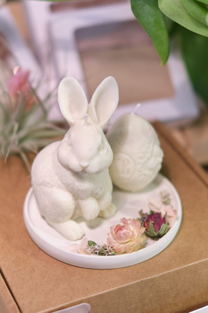 artisanal white rabbit candle and an Easter egg candle showcased on market stall during a festive event. Local markets or fairs promoting artisanal products. art of candle making and creative designsの写真素材