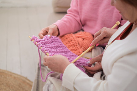 two older women knitting with natural wooden needles and environmentally friendly pink wool, demonstrating how knitting can be both a creative and sustainable hobby for people of all agesの写真素材