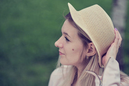 side view of a woman wearing a hat, displaying her distinctive birthmark on her cheek, adding...