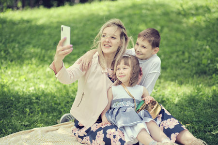 mother and her children document their special time in a park, using a smartphone for capturing memories. Balancing technology and personal connections in family life.の写真素材