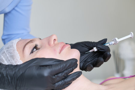 cosmetologist in sterile gloves, performing a precise chin prick with a hyaluronic acid filler. non-surgical options for facial contouring.の写真素材