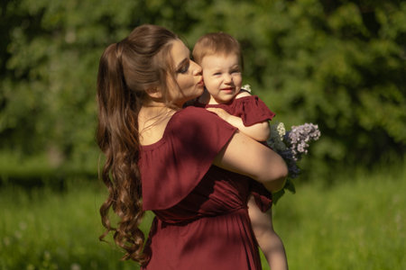 Family picnic in the park, a mother holding her young child and a fresh bouquet of lilac flowers during a sunny day. Concept: Outdoor Leisure Timeの写真素材