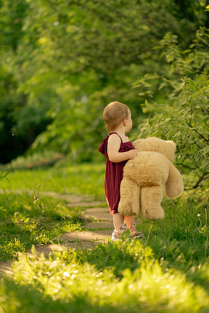 In the warm embrace of sunlight, a little girl and her fluffy bear find their own path in the parkの写真素材