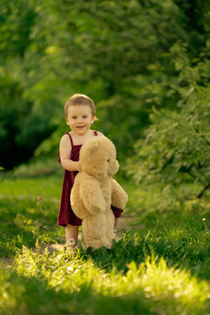 A year-old baby girl takes her first independent steps in a sunny park, clutching her teddy bear friendの写真素材