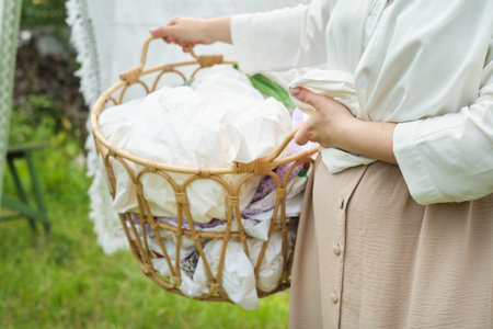 A photo of a woman holding a basket of freshly laundered clothes against the backdrop of an outdoor laundry line, reflecting the cleanliness and freshness achieved with the right laundry products.の写真素材