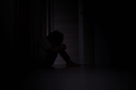 silhouette of a frightened boy who sits on the floor in a depressive phase, in a dark room