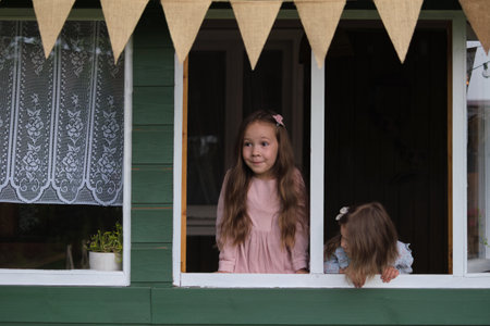 Set against a rustic green house, two young girls drink in the sights and sounds of a lush backyard garden, a testament to natures enduring beautyの写真素材