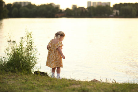 power of perspective and natural light in photography. A tiny girl holds a bouquet of daisies, her form silhouetted against a dramatic sunset over a calm lakeの写真素材