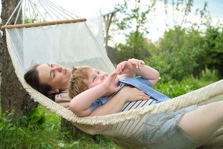 Wholesome Connection: A mother and son seize a perfect summer day to connect deeply, nestled in the haven of a backyard hammockの写真素材