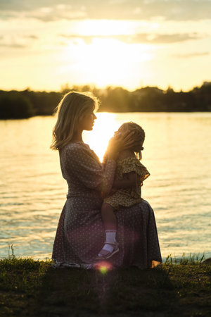 mom and her child hugging at sundown by lake epitomizes the rapeutic power of nature. warm hues of sunset symbolize mental solace that comes with close relationships and natural beauty.の写真素材