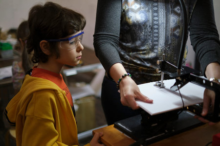 young boy meticulously carves wood on a lathe, under the careful guidance of his teacher. The image...