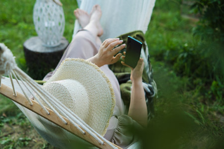 Mindful Multitasking: Woman in Hat Manages Digital Self-Care from the Comfort of Her Backyard Haven