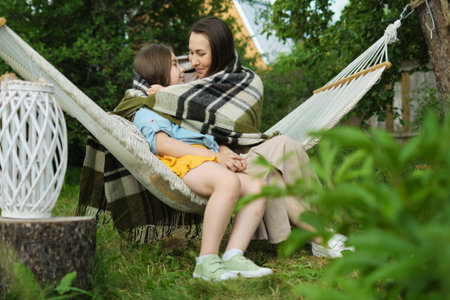 Embracing the new season, a loving mother and daughter share whispers and smiles in a floral-framed hammock.の写真素材