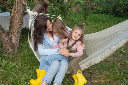 Loving mother and two little daughters share a warm embrace in a garden hammock, radiating happiness and familial bond.の写真素材
