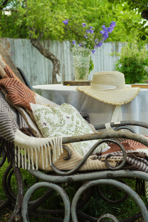 Nestled in a quiet garden, a cozy corner features a chair and a blanket, a table with bluebells, a straw hat, and a novel. The perfect retreat for reflection.の写真素材