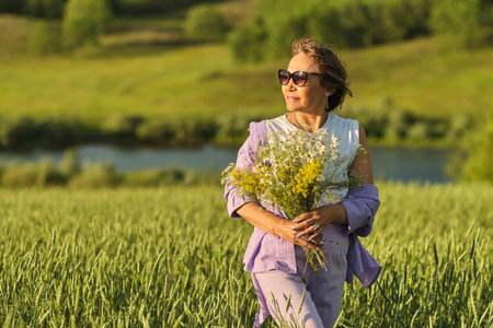 Elderly woman in stylish clothing relaxing in a lush meadow, embodying the fulfilling experiences offered in senior communitiesの写真素材