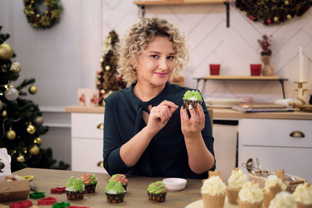 Engrossed in her work, the woman in green brings Christmas to her kitchen with cupcakes. For her, creativity meets confection in every design.の写真素材
