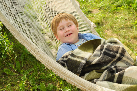 Boys joyful escape in a garden hammock, wrapped in comfort, smile radiating peace. A tranquil retreat from urban hustle, epitomizing serene childhood.の写真素材