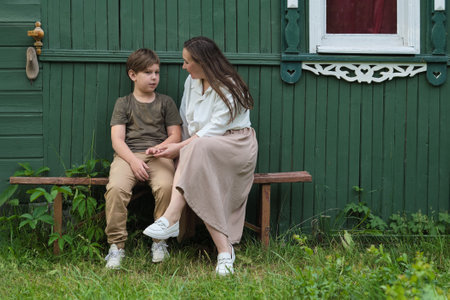 moment of familial support captured, as a mother seeks to lift the spirits of her distressed elementary-aged son, both seated by their home, underlining the bonds of familyの写真素材