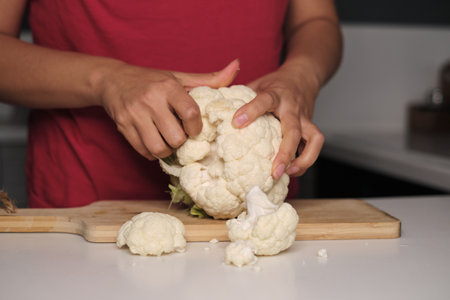 Feminine fingers snap fresh cauliflower into pieces, a culinary canvas forms. Dive into the home-cooking trend, making ordinary extraordinary.の写真素材