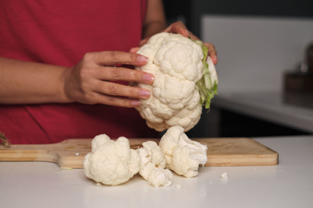 Soft hands tear vibrant cauliflower florets, a kitchen dance begins. Uncover the simple ways to infuse wellness in daily meals.の写真素材