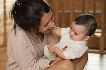 Home Sweet Home: A radiant mother savors a blissful moment as she hugs and kisses her toddler, illuminating a cozy wooden interior with her loveの写真素材