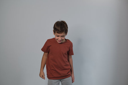 A joyful boy laughs, looking downwards in a casual rust-colored t-shirt and grey sweatpants. His genuine expression reflects a rising trend towards capturing authentic, unposed moments in photography.の写真素材