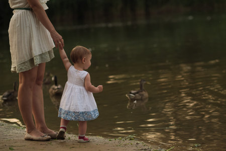 Calm waters and a mothers gentle hold create a peaceful scene, ducks in the backdrop. It illustrates the growing movement towards eco-conscious parenting.の写真素材