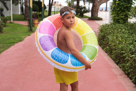 Youth heads towards sea, inflatable in tow, hinting adventure. Echoes the importance of play in natural settings.の写真素材
