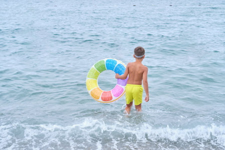 Youth heads towards sea, inflatable in tow, hinting adventure. Echoes the importance of play in natural settings.の写真素材