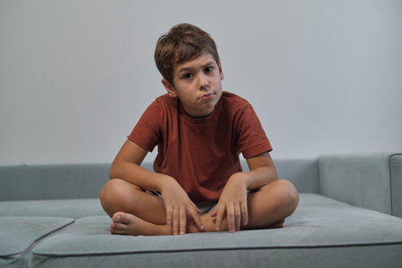 A boy sits, legs crossed, with a contemplative frown. His demeanor points to the nuanced emotions children navigate daily.の写真素材