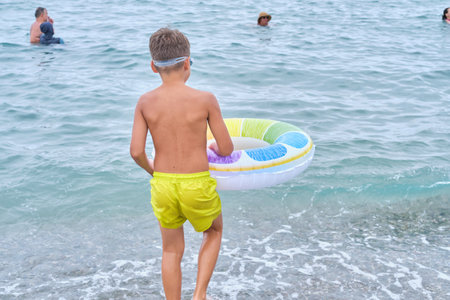 Child with float strolls down a path, sea beckoning. Reflects the allure of water play in summer leisure.の写真素材