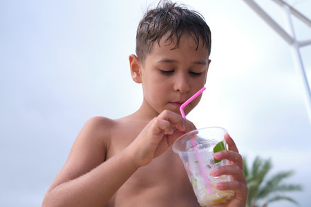 Youngster with inflatable ring sips a drink, beachgoers relax. This authentic shot highlights leisure and the simplicity of seaside enjoyment.の写真素材