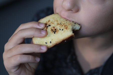 A young person nibbles on a toasted slice, sesame seeds sprinkled on top. Reflects the growing preference for homemade, wholesome meals over processed foodの写真素材