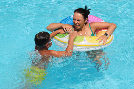 A boy grips a colorful float as his mother smiles; a sunny pool scene. This image ties to the joy of active parenting.の写真素材