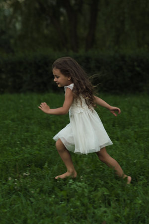 With a beaming smile, the girl dashes in the girls breezy attire, embodying innocence. The photo aligns with the eco-conscious trend promoting outdoor play over digital entertainment.の写真素材