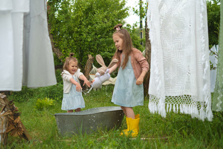 Wholesome fun: Sisters share a playful moment with a tub amidst nature and hanging laundryの写真素材