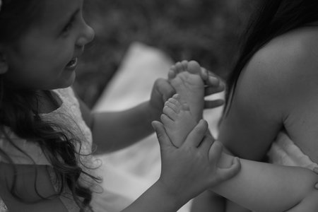 A girl gently holds a babys feet, symbolizing care and sibling love. This image resonates with themes of childhood and protectionの写真素材
