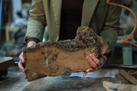 Hands hold a slab of burl wood with intricate grain, highlighting the natural artistry that...