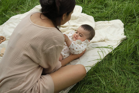 A baby giggles at mom s tickles on a blanket in the park. These joyful moments highlight the bond...