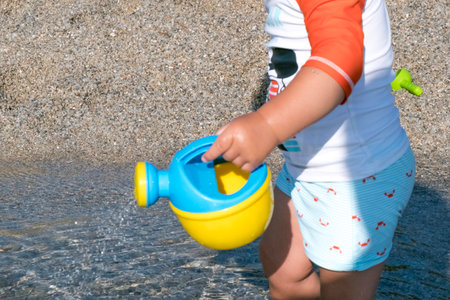 playing on the beach at the sunset time. baby playing with water on sea shore. closeup of the hand holding the watering can with waterの写真素材