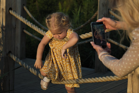 Girl on wooden bridge with ropes, with a dog nearby. Speaks to companionship and the joys of a...