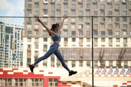 woman, dressed in blue athletic gear, leaps into the air on a track, showcasing her power and agility. benefits of explosive movements for building strength and cardiovascular fitness.の写真素材