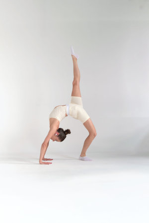 Woman in an elegant beige athletic outfit, performing a backbend in a bright studio. Concept:...