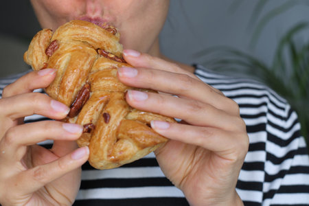 Persons mouth and hand biting into a pastry with pecans, showing a moment of indulgence. Concept:...